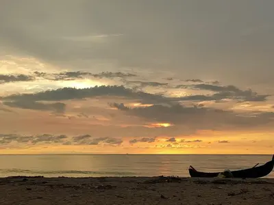 a boat on the beach with a sunset in the background at Coastal Den Homestay in Pallipuram