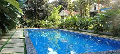 a blue swimming pool with a house in the background at Le Vista Resort in Sultan Bathery