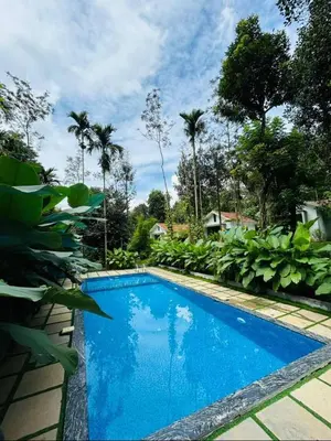 a blue swimming pool in a yard with palm trees at Le Vista Resort in Sultan Bathery