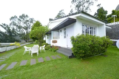 a small white house with two chairs in the yard at Sabol Holidays in Ooty