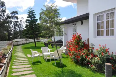 a yard with white chairs and flowers and a white house at Sabol Holidays in Ooty