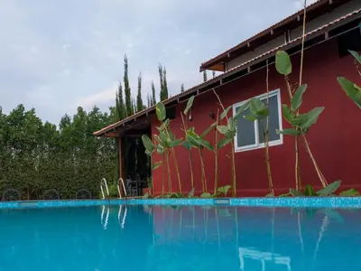 a red house with a swimming pool in front of it at Poojaris Nirantara - Mysuru in Hampāpura
