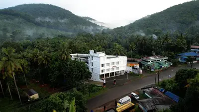 a white building on a street with a mountain at Sreeja Myst in Athirappilly