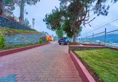 a car driving down a brick road with trees and a fence at Vintage Inglenook Premium Heritage Bungalow Ooty by VOYE HOMES - A Quiet Retreat Close to Ooty Town in Ooty