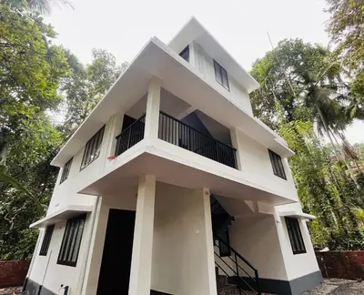 a white building with trees in the background at Montage Villa in Kozhikode