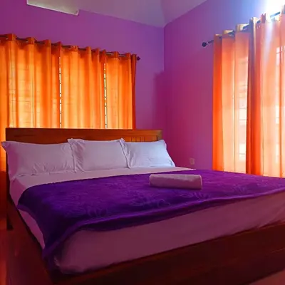 a bedroom with a bed with purple sheets and orange curtains at Wayanad Empire Budget Villa in Kalpetta