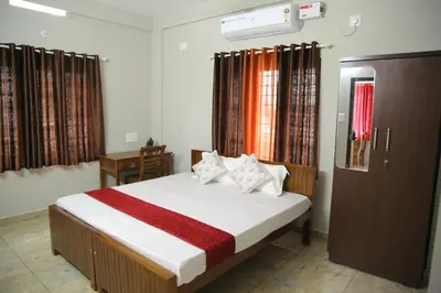 a bedroom with a bed and a desk and windows at NR HEAVENZ Near Rajagiri Hospital in Alwaye