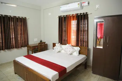 a bedroom with a bed and a desk and windows at NR HEAVENZ Near Rajagiri Hospital in Alwaye