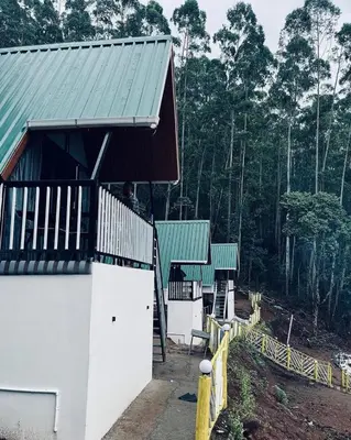 a white building with a green roof next to a forest at The Soul Of Vattavada in Vattavada