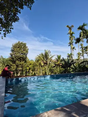 a man sitting next to a swimming pool with trees in the background at Churuli Bungalow in Ambalavayal