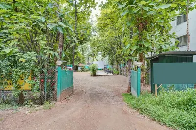 a dirt road with a green fence and trees at Super Townhouse Hebbal Mysore in Mysore