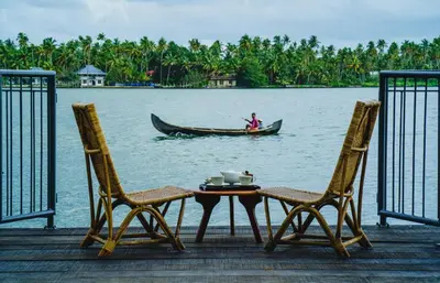 a table and two chairs and a man in a boat on the water at Vedic Village Retreat Kodungallur in Cochin