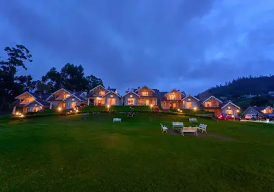 a large house with lights in a field at night at AJ Gable Clouds Ooty by VOYE HOMES - Serene Stay Near Avalanche Emerald Lake in Ooty