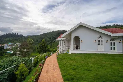 a white house with a green lawn in front of it at LohonoStays Villa Lansdowne in Coonoor