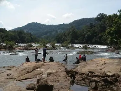 a group of people sitting on rocks in a river at Crystal Riverview Homestay in Kuttampuzha