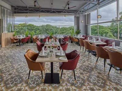 a restaurant with tables and chairs and large windows at Grand Continent Mysore A Sarovar Portico Affiliate Hotel in Mysore