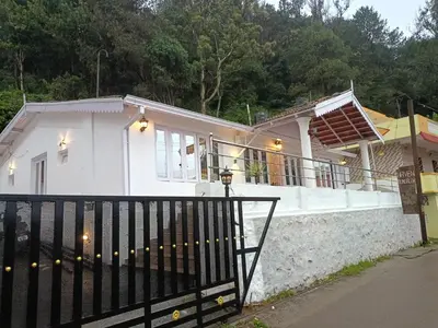 a white house with a black gate in front of it at Abbu Royal Palace Cottage in Ooty