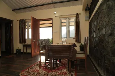 a dining room with a table and chairs and a stone wall at Wild and Free Farm Stay in Ooty