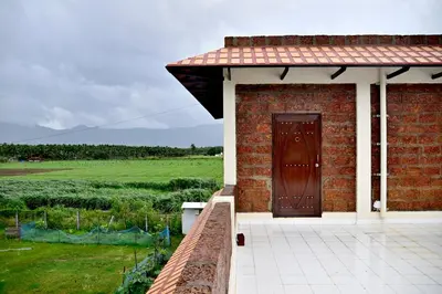 a brick house with a brown door and a field at Lakshmi illam Near Isha Yoga Adiyogi in Alāndurai