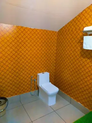 a bathroom with a toilet with an orange tiled wall at Bamboo Suite at Merlys Fruit Garden in Kotamangalam