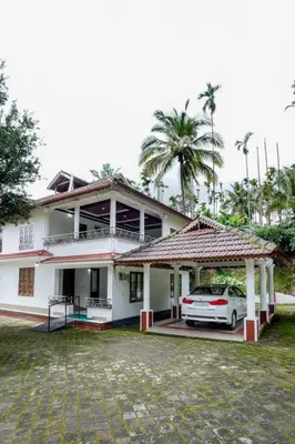 a white house with a car parked in front of it at Wayanad Palm Grove Retreat 1st Floor in Wayanad