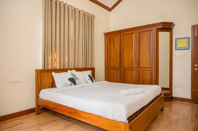 a bedroom with a bed with white sheets and wooden furniture at Puzhayoram holiday home, Aluva in Alwaye