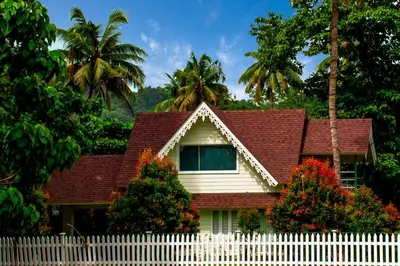 a white fence in front of a house with palm trees at River Wild holiday home in Athirappilly