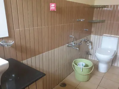 a bathroom with a toilet and a green bucket at Tropical Blooms by StayApart in Kutta