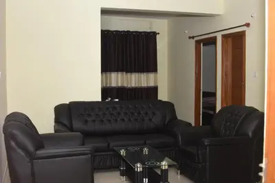 a living room with a black leather couch and a table at Golden Bells in Vānivilāsa Puram