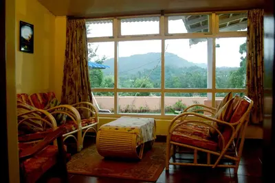 a living room with a large window and a table and chairs at Bella Vista Homestay in Coonoor