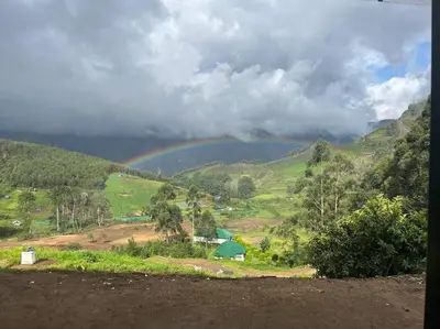 a rainbow over a hill with a farm and a field at Orange Valley Farm Resort in Munnar