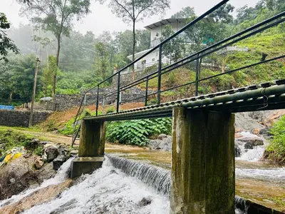 a bridge over a river with a waterfall at Brooke hills falls view in Vallikavungal