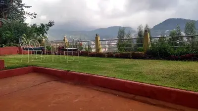 a yard with chairs and a fence with mountains in the background at Wyoming Heritage in Ooty