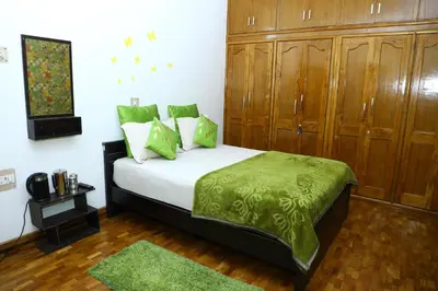 a bedroom with a bed with green sheets and wooden cabinets at Pine Hood Villa in Ooty