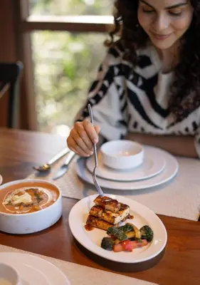 a woman sitting at a table with a plate of food at LohonoStays Amani Villa 9A in Coonoor