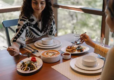 a woman sitting at a table with plates of food at LohonoStays Amani Villa 9A in Coonoor