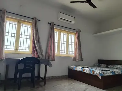 a bedroom with a bed and a chair and windows at MMVK Homestay AC, Spacious & Comfortable Entire Home Just For You in Pollāchi