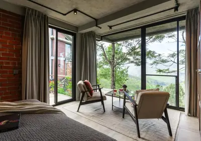 a bedroom with a bed and chairs and large windows at LohonoStays Amani Villa 10A in Coonoor