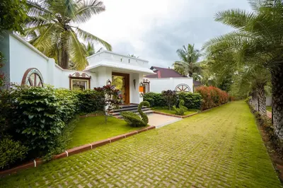 a white house with a green lawn and palm trees at Regenta Resort Mysore Tropical Village in Chāmundi