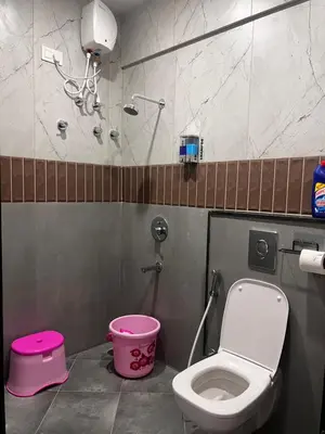a bathroom with a toilet and a pink bucket at SAHARHOMEstay O3 in Mysore