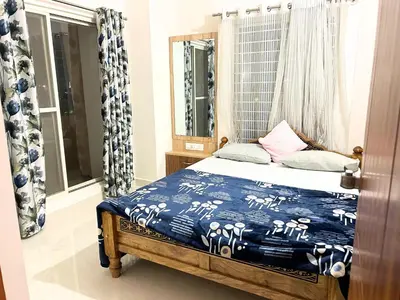 a bedroom with a bed with a blue comforter and a window at Mannat Inn Classic Premium - 3BHK in Mysore