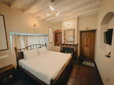 a bedroom with a bed with white sheets and a fireplace at The Humming Bird A Stay Chapter in Ooty