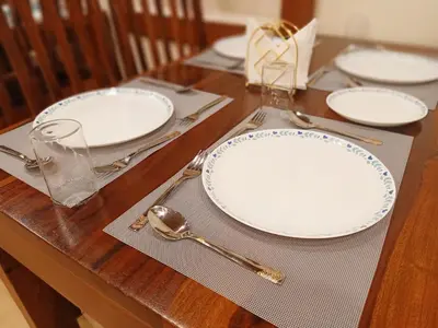 a wooden table with white plates and silverware on it at The Humming Bird A Stay Chapter in Ooty
