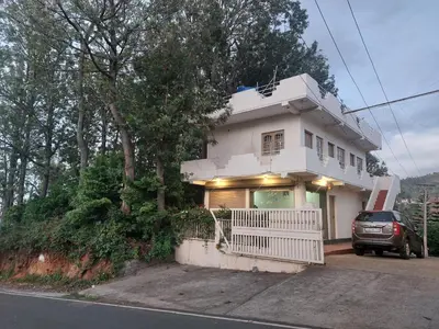 a white house with a car parked in front of it at GEM Stays in Ooty