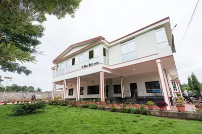 a white house with a green yard at Bota Royal in Kushālnagar