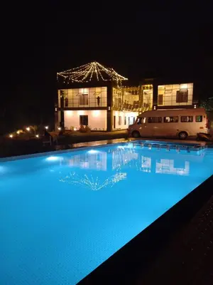 a large blue swimming pool in front of a building at night at Mountain Wings Resort in Vythiri