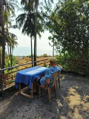 a man sitting at a table in front of the ocean at Perch Next door in Kannur