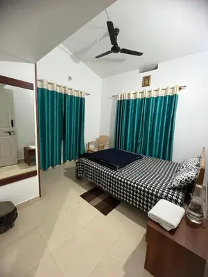 a bedroom with a bed with green curtains and a mirror at GURI Homestay in Kushālnagar