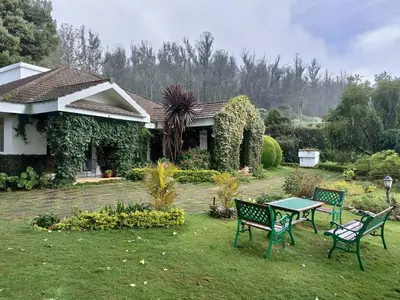 a house with two chairs and a table in the yard at Hideaway in Ooty