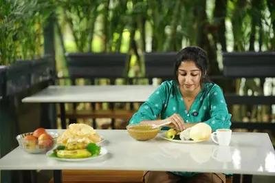 a woman sitting at a table with a plate of food at Ayurnest Pool Resort Wayanad in Batheri